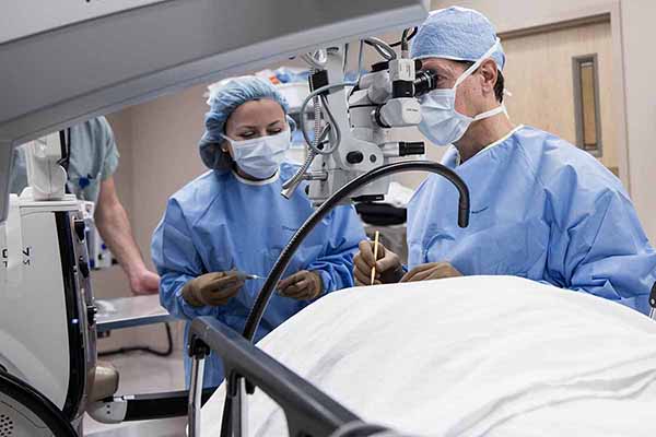 Doctor looking through medical equipment while he and the nurse perform a  medical procedure on the patient’s eye.